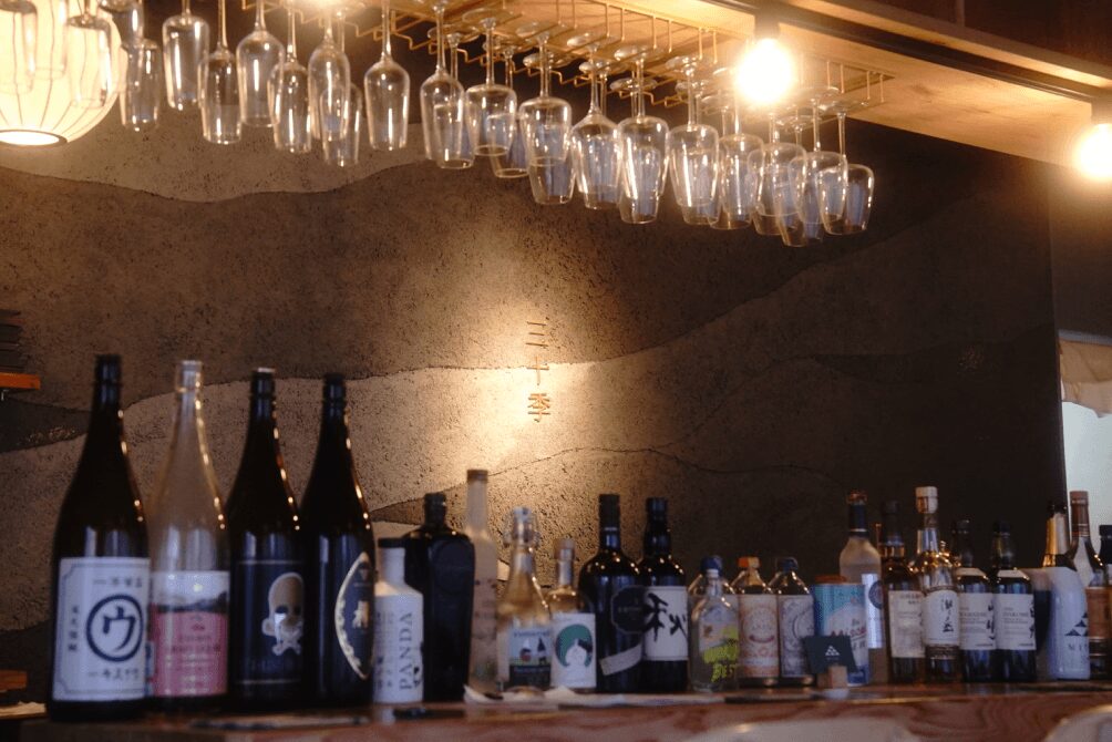 美しく吊り下げられたワイングラスと、壁面に「三十季」の文字が光るカウンター