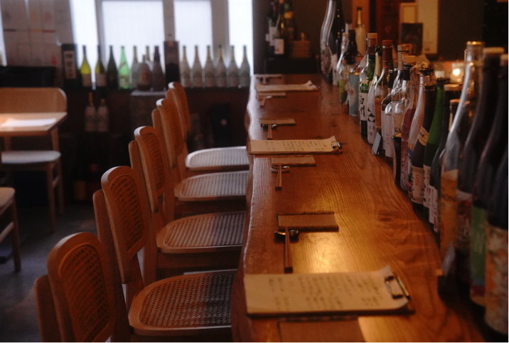 木目が美しい一枚板のロングカウンターと、整然と並ぶこだわりのお酒