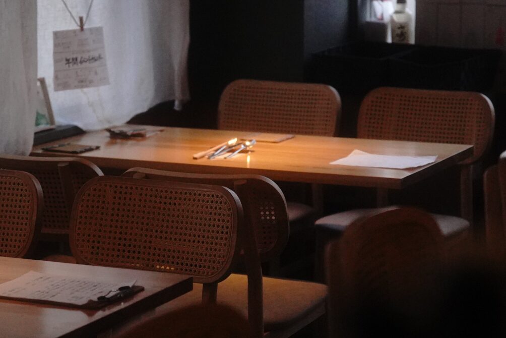 温かい光が差し込む、落ち着いた雰囲気の木製テーブル席とラタンチェア