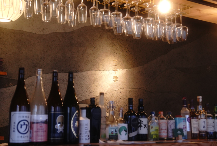 美しく吊り下げられたワイングラスと、壁面に「三十季」の文字が光るカウンター