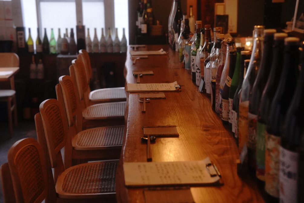 木目が美しい一枚板のロングカウンターと、整然と並ぶこだわりのお酒