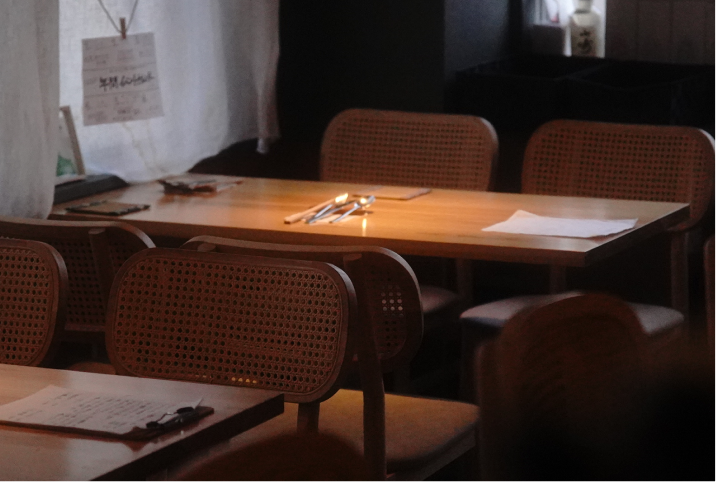 温かい光が差し込む、落ち着いた雰囲気の木製テーブル席とラタンチェア